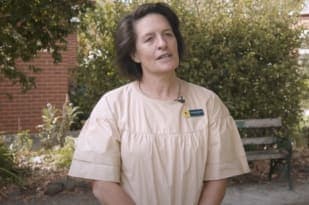 A teacher in a white shirt and nametag looks at the camera.