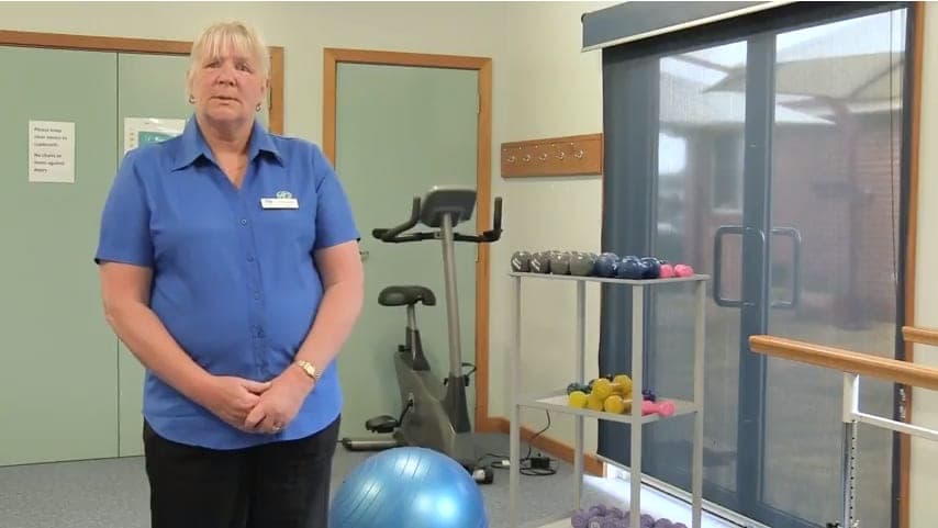 A woman in a blue shirt stands in a room filled with gym equipment