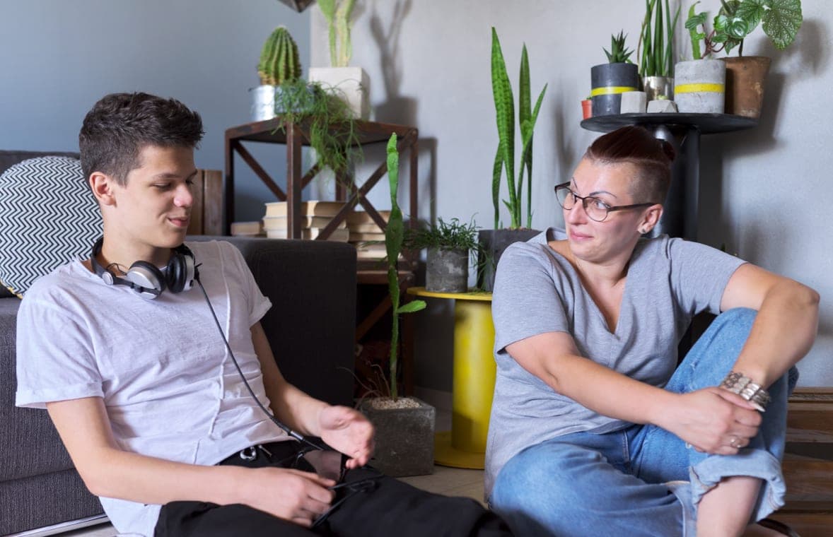 A parent sitting on the floor next to a teenager