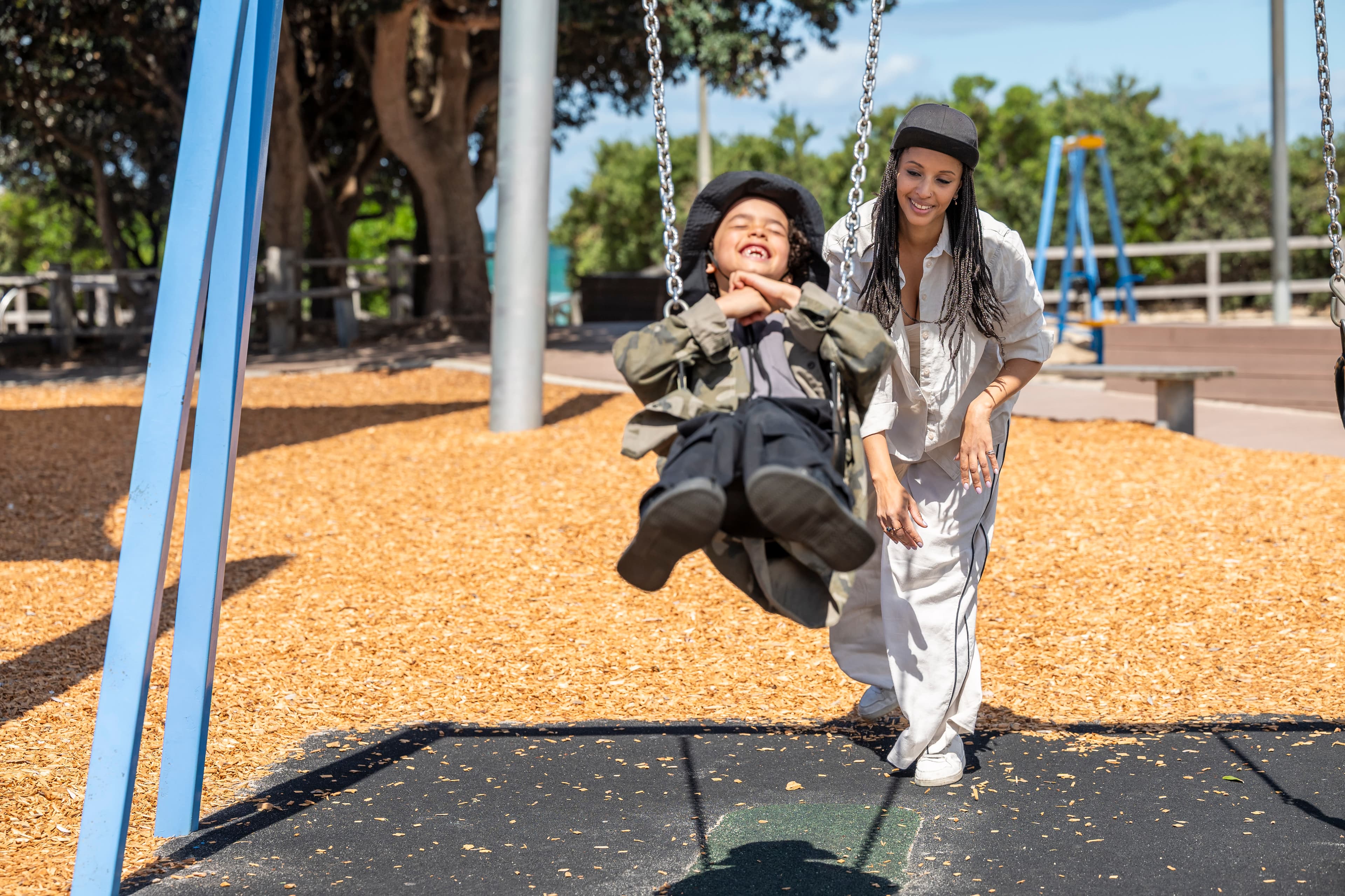 A woman pushes a child on a swing at a playground.